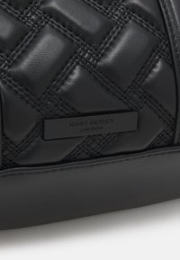 Borsa in pelle nera trapuntata con un'etichetta metallica rettangolare nera sul lato, che riporta in rilievo la scritta "Kurt Geiger London".