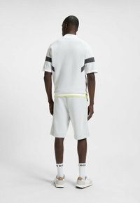Korte mouwen, wit getextureerd gebreid shirt met donkere strepen, gecombineerd met lichtgrijze shorts. Heeft een minimaal ontwerp, een relaxte pasvorm en schoeisel met accenten.