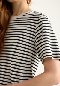Schwarz-weißer kurzärmeliger T-Shirt mit rundem Ausschnitt; der Stoff wirkt weich und leicht. Das Muster ist durchgängig einheitlich.