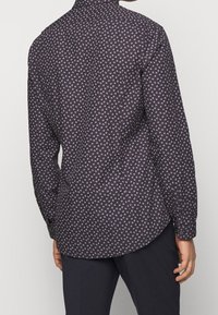 Langsleeve shirt in donkerpaars met een klein, herhalend wit bladpatroon. Heeft een traditionele kraag en knoopmanchetten.