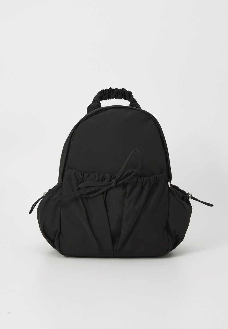 Black fabric backpack with a rounded shape, gathered detailing at the bottom, elasticized top handle, and side zippers for closure.