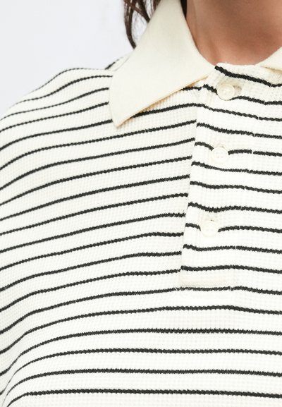 Biele polo tričko s čiernymi pruhmi, textúrovaná látka, krátky golier a tri biele gombíky na límci.