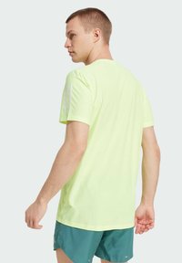 Camiseta deportiva de color amarillo neón con cuello redondo, mangas cortas y rayas acentuadas en blanco en el hombro izquierdo. Tejido texturizado y corte holgado.