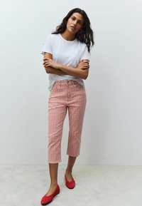 Witte t-shirt met korte mouwen, gecombineerd met rode en witte geruite cropped broek en rode platte schoenen. Eenvoudig ontwerp en een gladde stoftextuur.