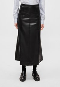 Fekete bőrmáxi szoknya függőleges varrásokkal és oldalsó sliccel. Világoskék inggel és fekete mokaszin cipővel párosítva. Simogató textúra, testhez simuló sziluett.