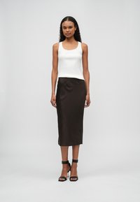 Witte geribde tanktop gecombineerd met een bruine satijnen midi rok, met een gladde textuur en een aansluitende silhouet. Zwarte enkelsandalen met bandje maken de look compleet.