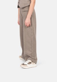 Pantaloni a gamba larga marrone chiaro realizzati in tessuto morbido con una superficie liscia. Indossati con sneakers beige con design a stampa leopardo.