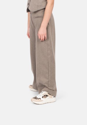 Hellbraune, weite Hosen aus weichem Stoff mit glatter Textur. Getragen mit beigen Sneakers, die ein Leopardenmuster-Design aufweisen.
