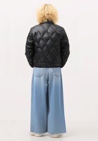 Giubbotto imbottito nero con trapuntatura e alto colletto, abbinato a pantaloni in denim larghi di colore blu chiaro. Tessuto morbido, vestibilità rilassata, dettagli di cucitura visibili.