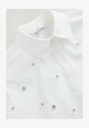 Biela košeľa na gombíky s klasickým golierom, zdobená roztrúsenými kamienkami rôznych veľkostí na prednej strane.