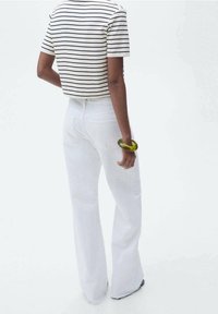 Jeans bianchi a gamba larga con vita alta, abbinati a un top a righe in bianco e nero, corto. Un bracciale circolare verde è indossato al polso.