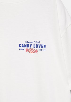 Biele tričko s modrým textom „Sweet Club CANDY LOVER Sugar Society“ a ružovou pruhovanou cukrovinkou uprostred na hrudi.