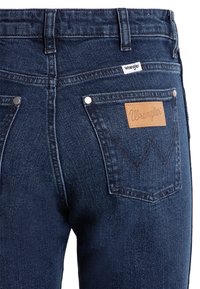 Donkerblauwe Wrangler denim jeans met een recht afgesneden beenontwerp, leren logo patch, zilveren klinknagels en een klassiek stikselpatroon op de achterzakken.