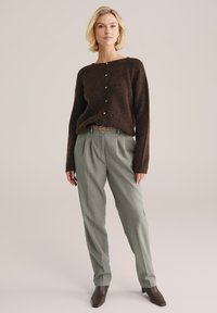 Pulover tricotat texturat maro cu închidere cu buton, asortat cu pantaloni eleganți gri deschis și cizme cu toc negre până la gleznă.