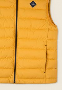 Żółta kamizelka ocieplana o pikowanej fakturze, z zamkiem błyskawicznym z przodu i czarną naszywką z logo. Bez rękawów, wykonana z lekkiego materiału syntetycznego.
