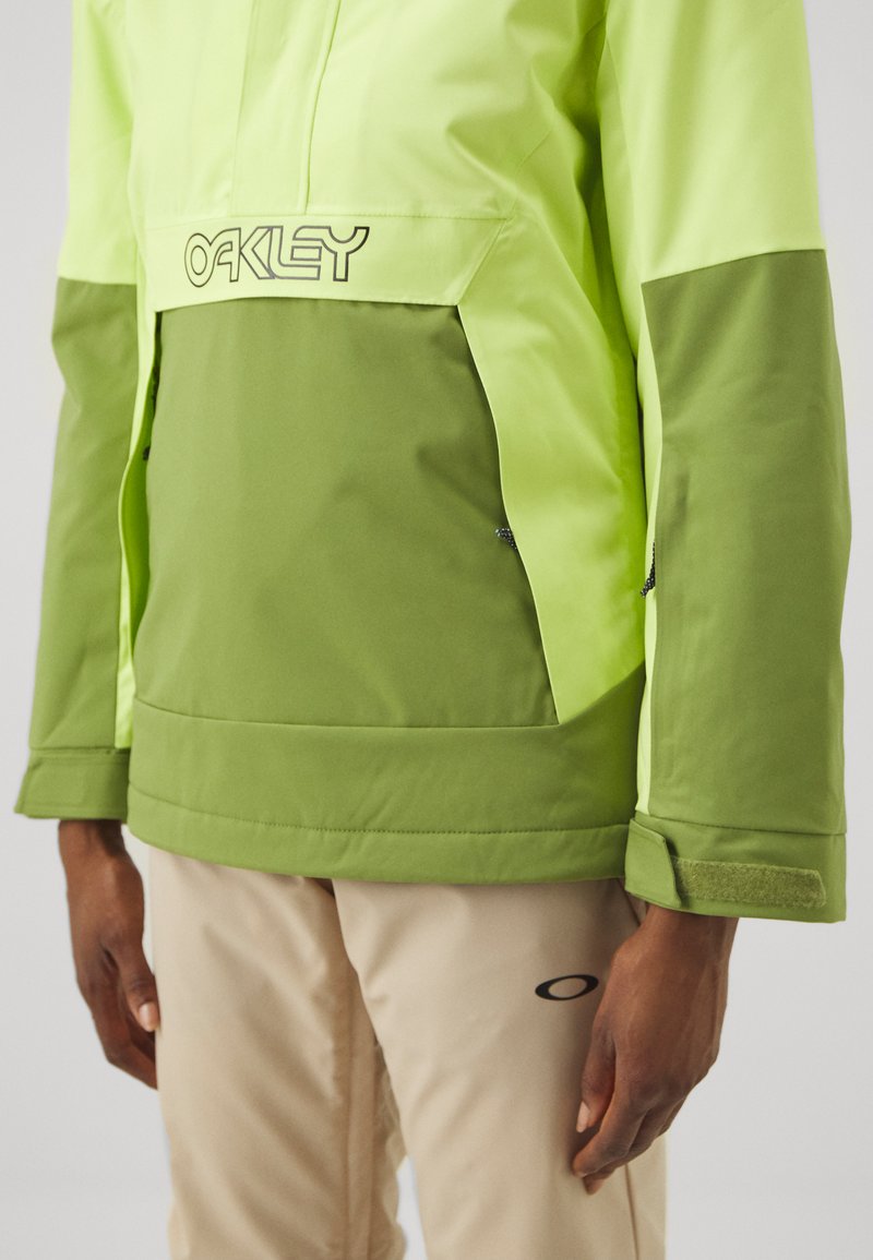Grön och neongul jacka med dragkedja fram, Oakley-logotyp på bröstet och kardborreaccenter. Slätt, texturerat tyg med lagerdesign.