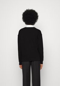 Felpa nera con scollatura rotonda, maniche lunghe e polsini a costine, abbinata a pantaloni scuri e larghi. Design semplice, senza fantasie.