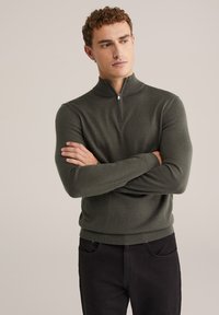 Pulover ales, de culoare verde măsliniu, cu un guler înalt și o închidere cu fermoar scurt. Textură tricotată, mâneci lungi și manșete și tiv cu densitate.