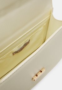 Borsa in pelle beige con chiusura dorata, tasca interna in tessuto beige e etichetta "ANNA FIELD" all'interno.