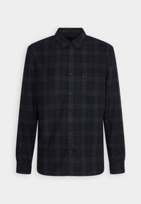 Chemise à manches longues à carreaux noir et vert foncé, boutonnée avec col et poche poitrine, présentée sur un fond blanc uni.
