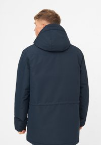 Chaqueta aislante de color azul marino con una gran capucha, que presenta una textura suave y un corte ligeramente más largo con detalles cosidos en la parte posterior.