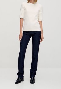 Valkoinen lyhythihainen paita yhdistettynä tummansinisiin kapeisiin farkkuihin. Asusteena mustat nilkkurit. Yksinkertainen ja siisti muotoilu.