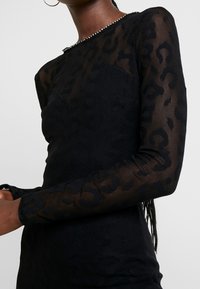 Haut à manches longues noir avec imprimé léopard texturé et transparent. Doté d'un col rond orné de petites clous décoratifs.