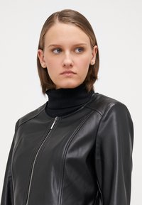 Black leather jacket with a zip closure and round neckline, featuring a ribbed black turtleneck underneath. Smooth texture, fitted design.