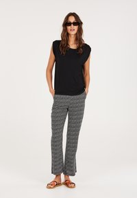 Top nero a maniche corte con scollatura rotonda, abbinato a pantaloni a palazzo neri e bianchi a fantasia e sandali marroni. Modella con occhiali da sole.