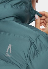 Turkusowa kurtka puchowa o miękkiej, gładkiej teksturze, z wysokim kołnierzem i logo z napisem "TECHNOLOGIA BEZPIECZEŃSTWA" w szarym kolorze.