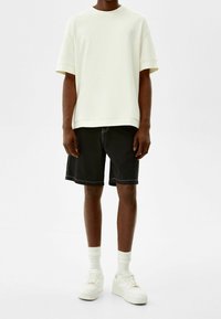 Valkoinen ylisuuri t-paita, mustat shortsit, joissa on valkoiset ompeleet, ja valkoiset lenkkarit paksuilla pohjilla, jotka on varustettu ribbikuvioidulla pyöreällä kaula-aukolla ja hihansuilla.