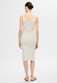 Robe midi en maille beige clair avec une silhouette ajustée. Caractérisée par de larges bretelles et un dos en V, mettant en valeur une finition côtelée texturée.