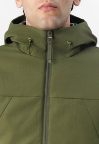 Olivgrüne Jacke mit strukturiertem Design, ausgestattet mit hohem Kragen, Reißverschluss, verstellbarem Kordelzug-Kapuze und strukturiertem Stoff.