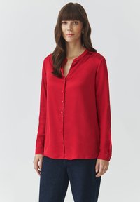 Red silk shirt with a button-down front, long sleeves, rounded hem, and small collar. Smooth texture with a subtle sheen.