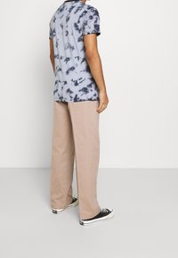 Camiseta de manga corta de tie-dye en azul y gris, combinada con pantalones beige sueltos y zapatillas negras, vista desde atrás.