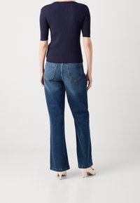 Granatowy prążkowany top z krótkim rękawem w połączeniu z luźnymi, średnio niebieskimi dżinsami, posiadającymi tylne kieszenie i delikatne wyblaknięcie, uzupełnione beżowymi szpilkami.