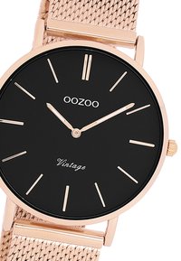 Montre à cadran noir avec un bracelet en maille rose doré. Elle présente des marqueurs d'heure minimalistes, le nom de la marque "OOZOO" et le texte "Vintage" en écriture élégante.