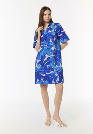 Kurzes Kleid mit blau-weißem Blumenmuster, Kragen, leichtem Stoff, knielanger Schnitt und kombiniert mit beigen Absatzsandalen.