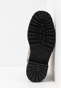 Semelle de botte en caoutchouc noir avec des crampons profonds et une finition texturée. Présente une forme arrondie et des bords lisses, étiquetée avec la taille 39.