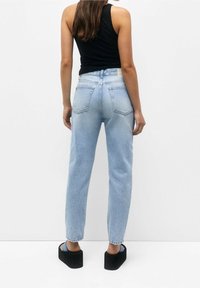 Ljust blå högmidjade jeans med rak passform, bakfickor och fransade fållar, kombinerat med svarta platåsandaler och en svart linne.