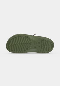 Подметка на маслиненозелен обувка Crocs, показваща текстуриран шарен протектор и лого Crocs, дебосирано в центъра.