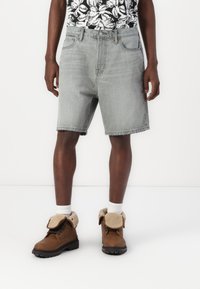Lysegrå denimshorts med lige snit og rå kant, parret med brune støvler med en fyldig krave og mørke gummisåler.