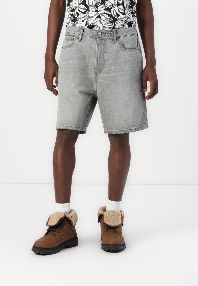 Lysegrå denimshorts med lige snit og rå kant, parret med brune støvler med en fyldig krave og mørke gummisåler.