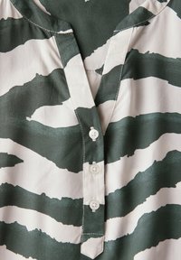 Blusa a rayas verdes y blancas con escote en V, frente botones y tejido suave. Presenta rayas onduladas y abstractas en toda su superficie.
