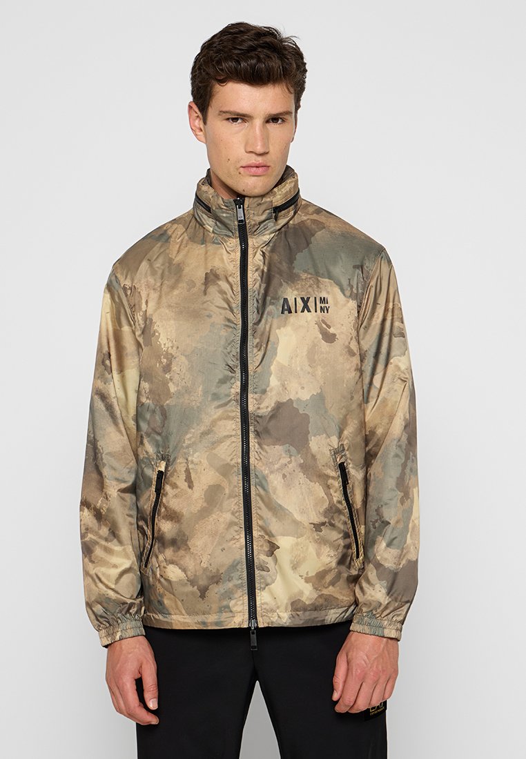 Camo-patroon windbreaker jack in beige en groene tinten, met een hoge kraag, rits aan de voorkant en zijzakken. Logo op de borst.