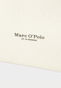 Biely plátený vak s nápisom "Marc O'Polo" vytlačeným čiernou farbou. Má hladkú textúru a minimalistický dizajn.