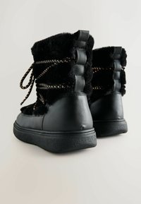 Schwarze Knöchelstiefel mit einem fellähnlichen Obermaterial und Lederakzenten, dekorativen Schnürsenkeln und einer strukturierten Gummisohle.