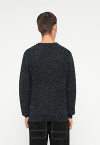 Suéter de punto azul marino con acabado texturizado, cuello redondo y dobladillo acanalado. Presenta mangas largas y un corte relajado.