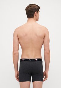 Sivé boxerky s čiernym elastickým pásom s logom "Champion". Tkanina vyzerá hladko a elasticky.