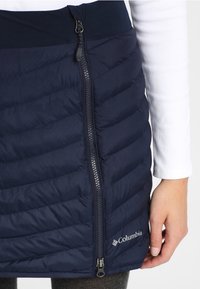 Marinblå isolerad kjol med quiltad design, framdragkedja och Columbia-logotyp. Mjuk tyg med ett stretchigt midjeband för komfort.